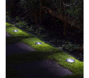 Aan de zijkant van een tuinpad zitten 4 grondspots in de tuin geduwd. 