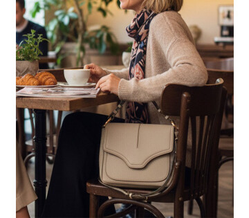 Beige DSTRCT Floater Field schoudertas aan een stoel in een café tijdens een koffiemoment.